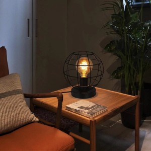 Schwarze Vintage Tischlampe mit rundem Metallkäfig und leuchtender E27 Glühbirne auf Holztisch. Ideal als Nachttischlampe.