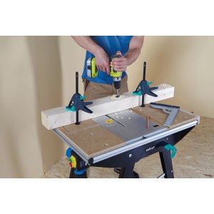 Werkstück fixiert mit wolfcraft Werktischspanner Pro auf Werktisch mit Bohrmaschine in Aktion.