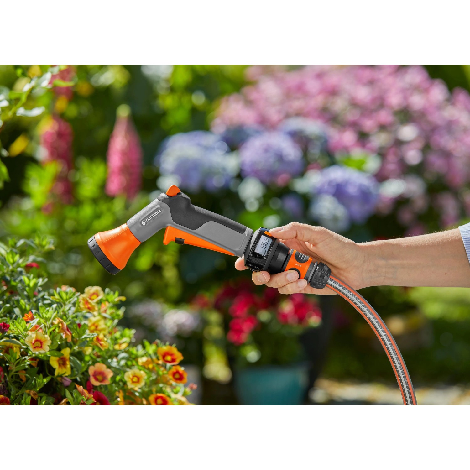Gardena AquaCount Bewässerungsbrause in Nutzung, mit digitaler Anzeige und orangefarbenem Sprühkopf.