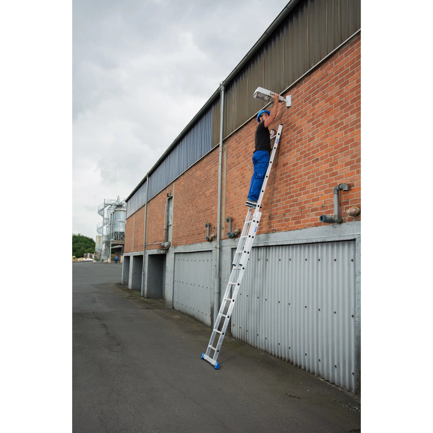 Krause Schiebeleiter Stabilo im Einsatz: Mann auf 2-teiliger Leiter an einer Hauswand.