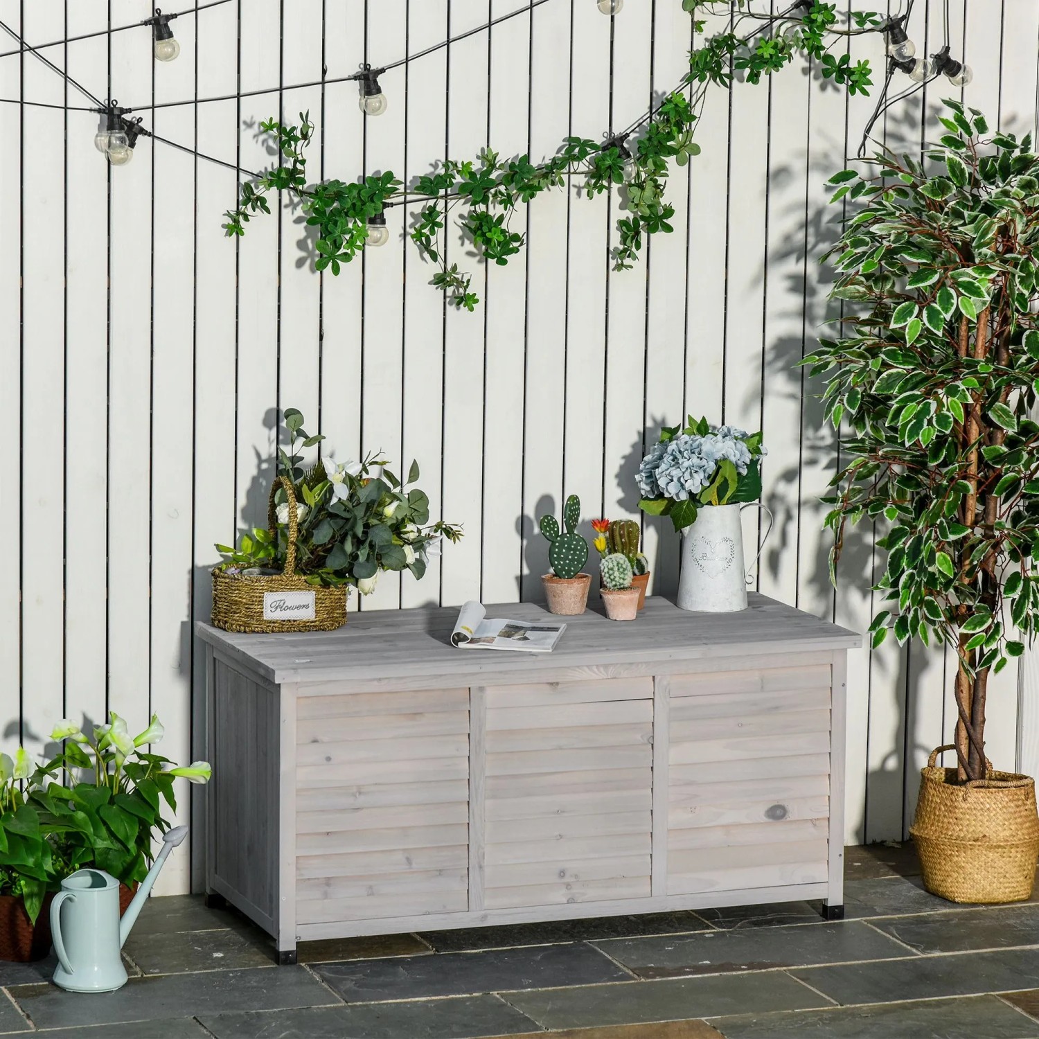 Graue Outsunny Gartenbox aus Holz mit Lamellenfront auf Terrasse. Wetterbeständige Aufbewahrungsbox, auch als Ablage nutzbar.