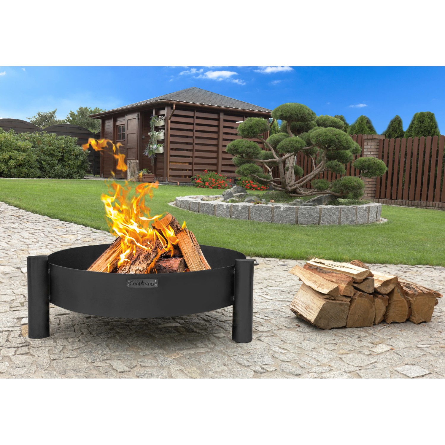 Schwarze CookKing Feuerschale Haiti (Ø 68cm) mit Feuerholz im Garten.