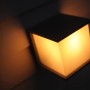 Leuchtende, anthrazitfarbene Lutec Box Cube Außenwandleuchte im Dunkeln.