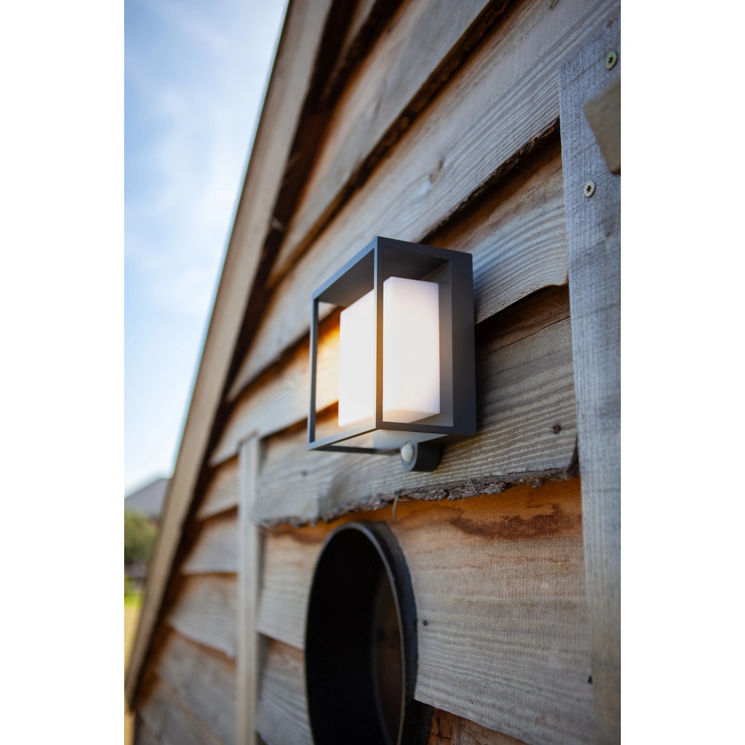 Moderne Lutec LED Solar-Wandleuchte Curtis mit Bewegungsmelder an einer Holzwand.