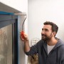 Mann streicht Fassade mit Farbroller, Fenster abgeklebt mit Tesa Malerband Professional Outdoor.