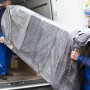 Möbeltransport: Zwei Träger hieven Möbelstück, geschützt mit Primaflor Möbelpackdecke, aus Transporter.