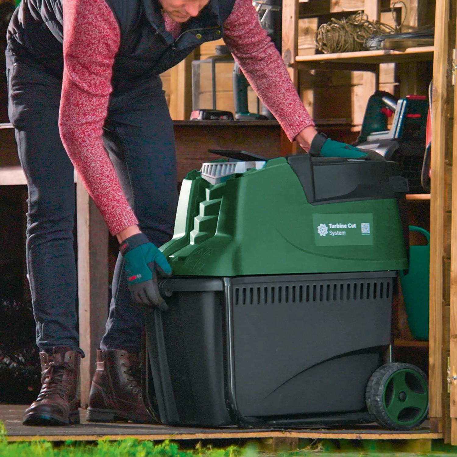 Bosch Gartenhäcksler AXT 25 TC in Grün/Schwarz mit Bediener vor Holzschuppen.