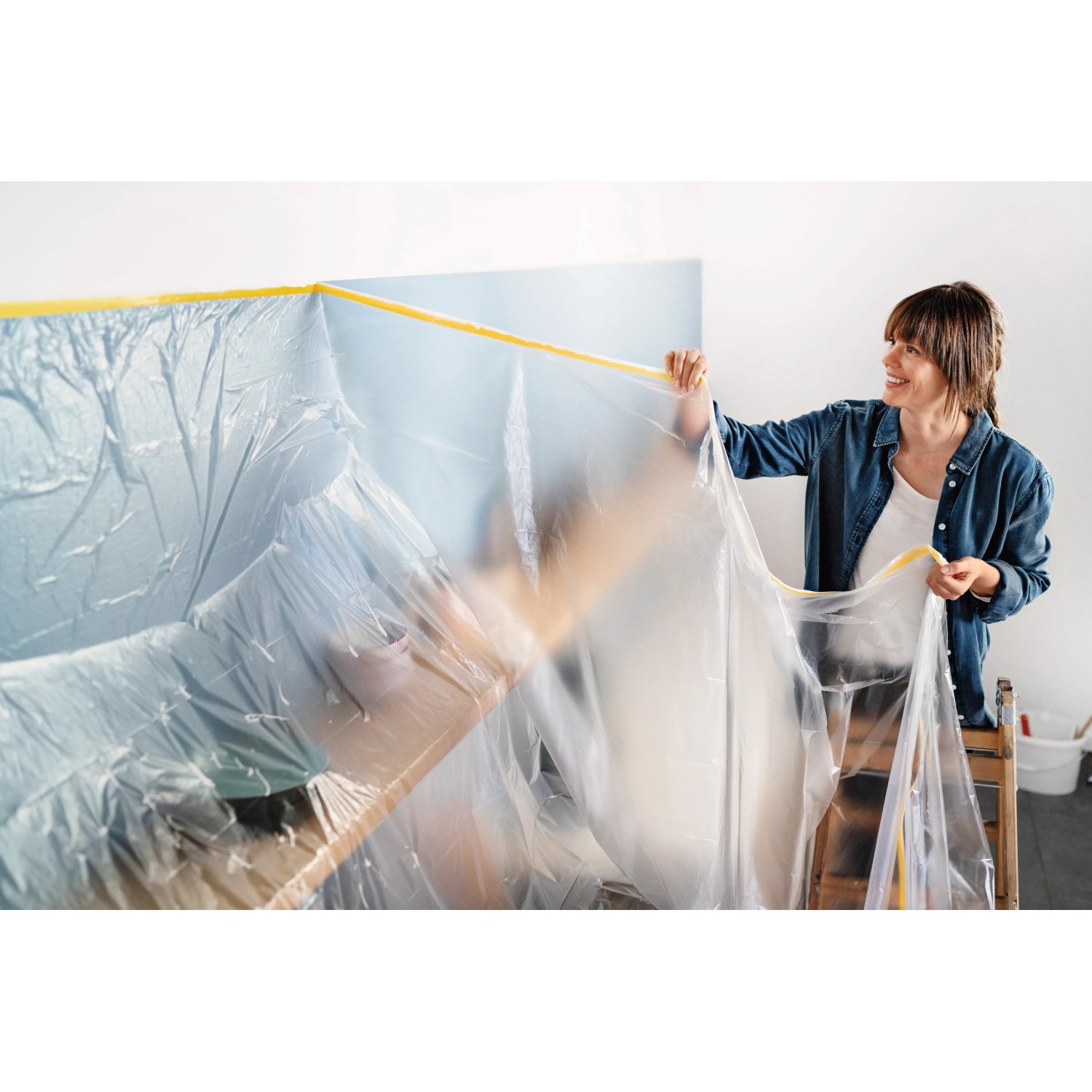 Frau bringt Tesa Abdeckfolie mit Klebeband Easy Cover Perfect+ M an Wand an.