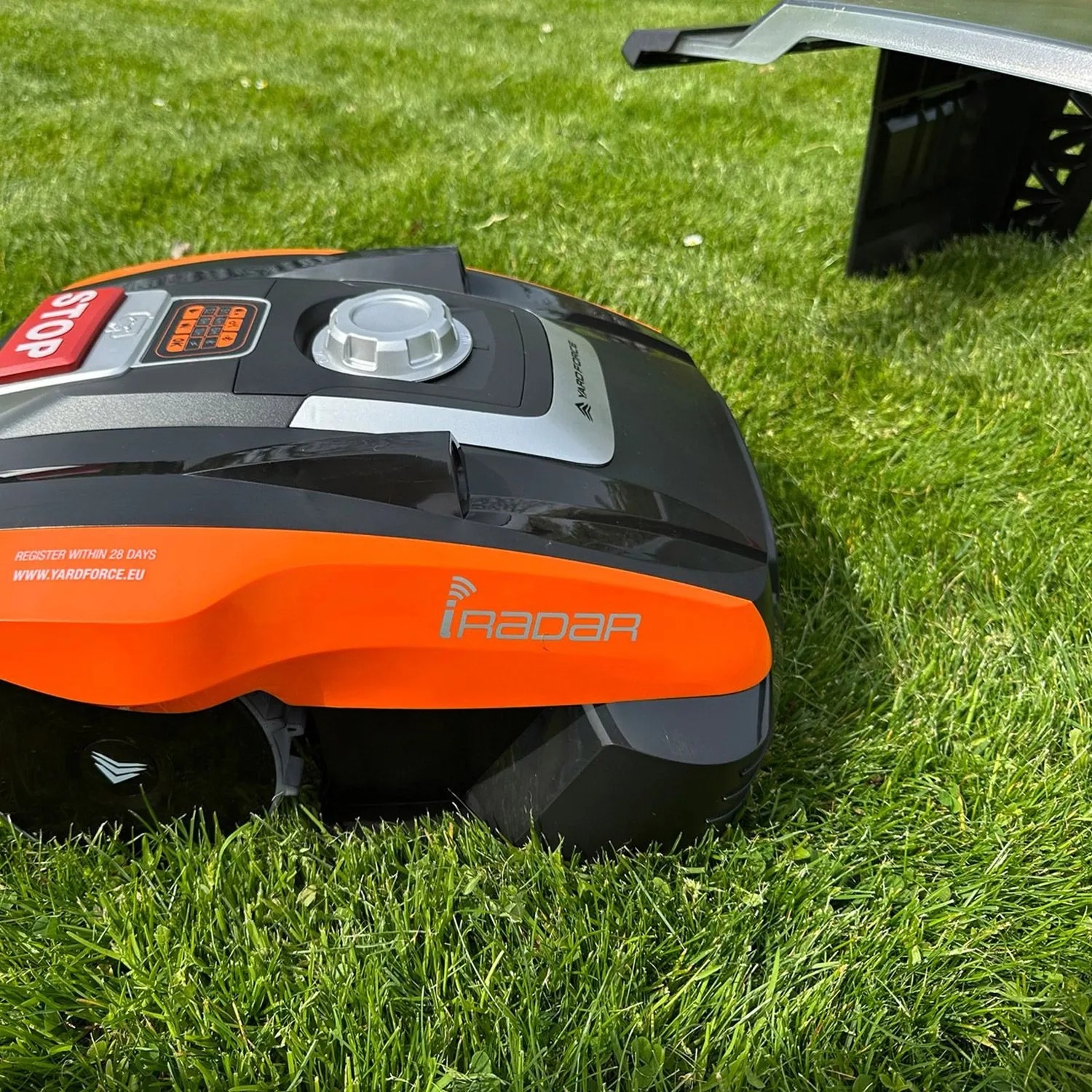 YARD FORCE Mähroboter Compact 300RBS auf grünem Rasen, orange-schwarz, mit iRadar Logo und Mähroboter-Garage.