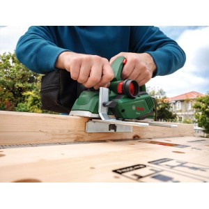 Hände führen grünen Bosch Elektrohobel PHO 20 über Holzbrett. Präzises Hobeln für glatte Oberflächen.