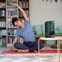 Grüner Bosch Akku-Bluetooth-Box UniversalSpeaker 18V-1 auf Tisch, Person macht Yoga. Kabelloser Lautsprecher.