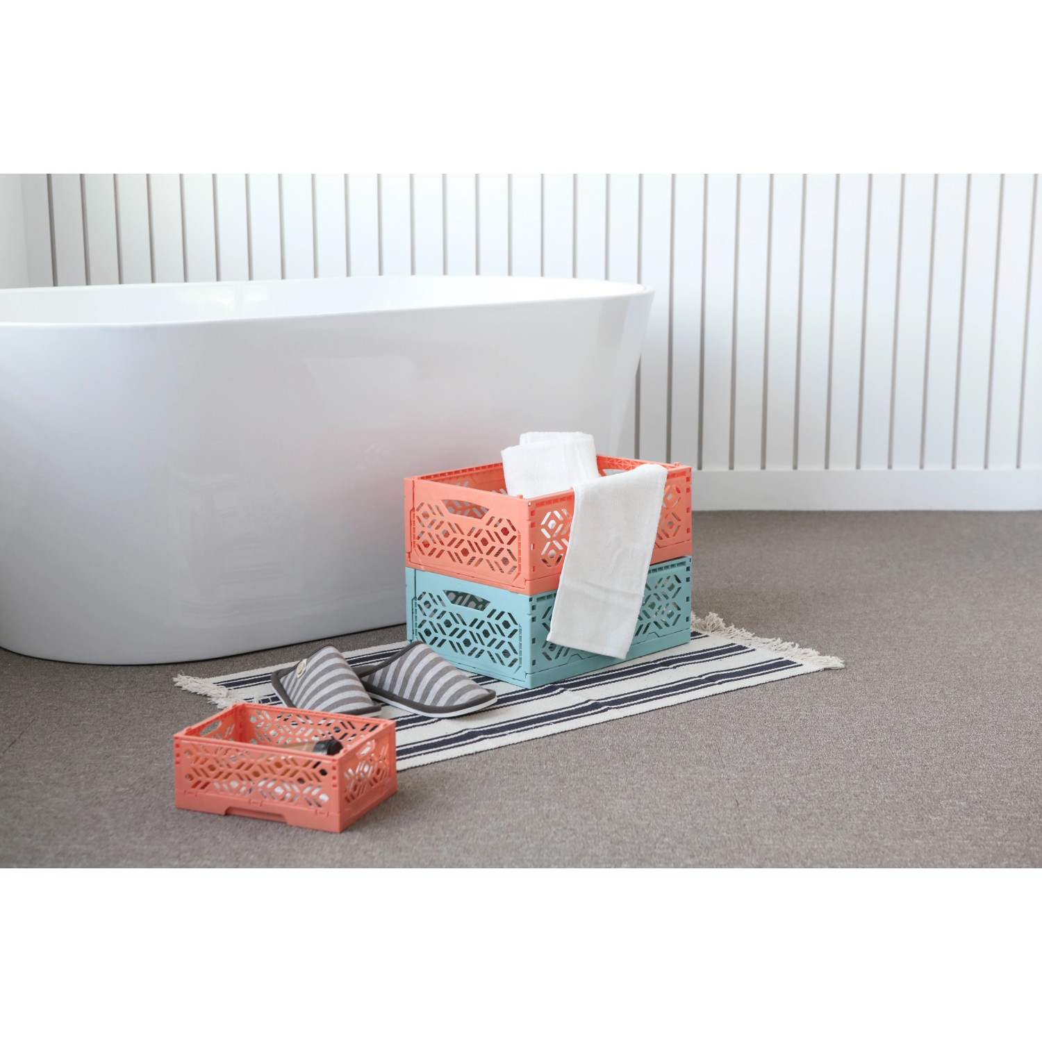 Türkisfarbene Klappbox-Mini und orangefarbene Box gestapelt im Badezimmer mit Handtüchern.