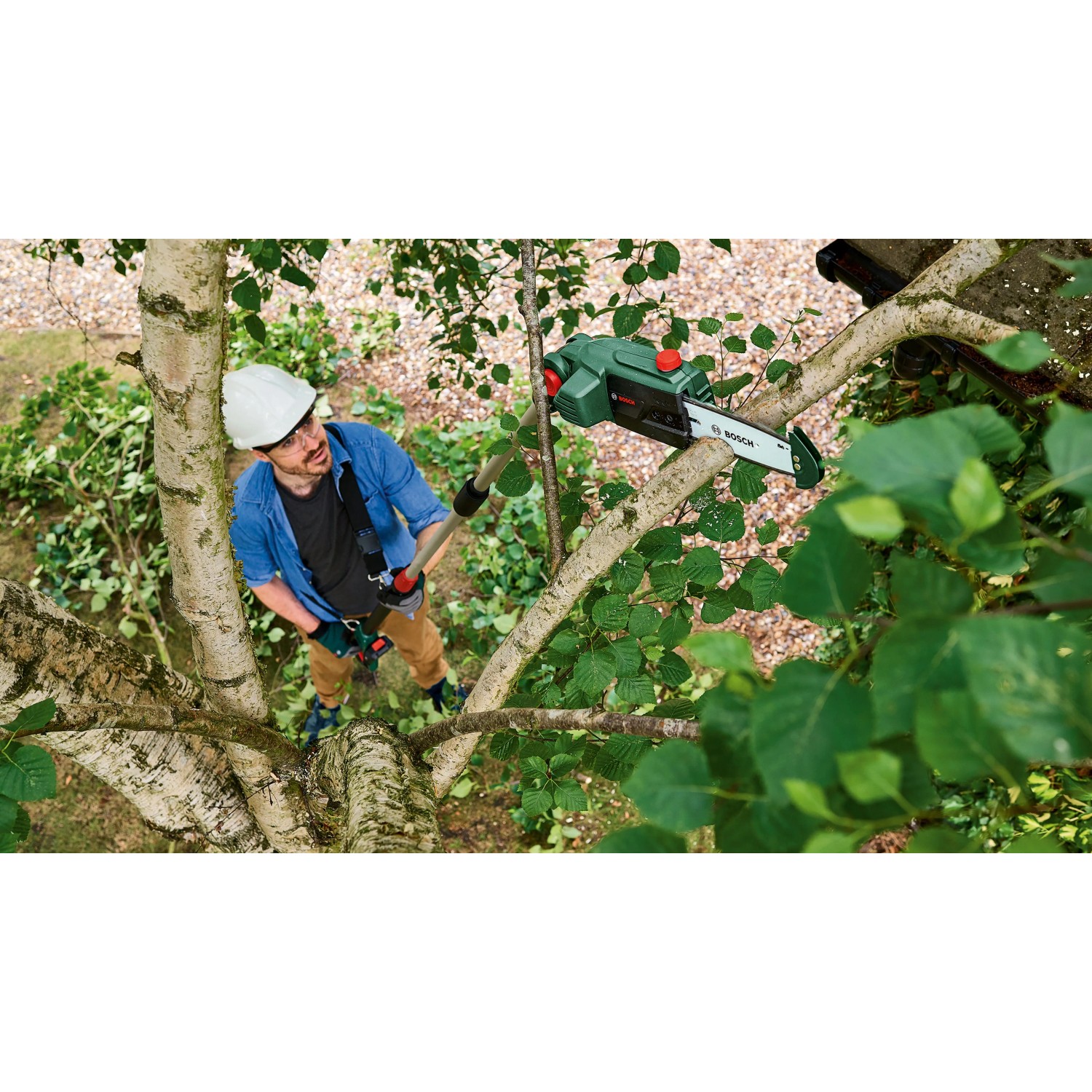 Mann mit Schutzhelm sägt Ast mit Bosch Akku Teleskop-Kettensäge. Kabelloser Hochentaster für Baumpflege.
