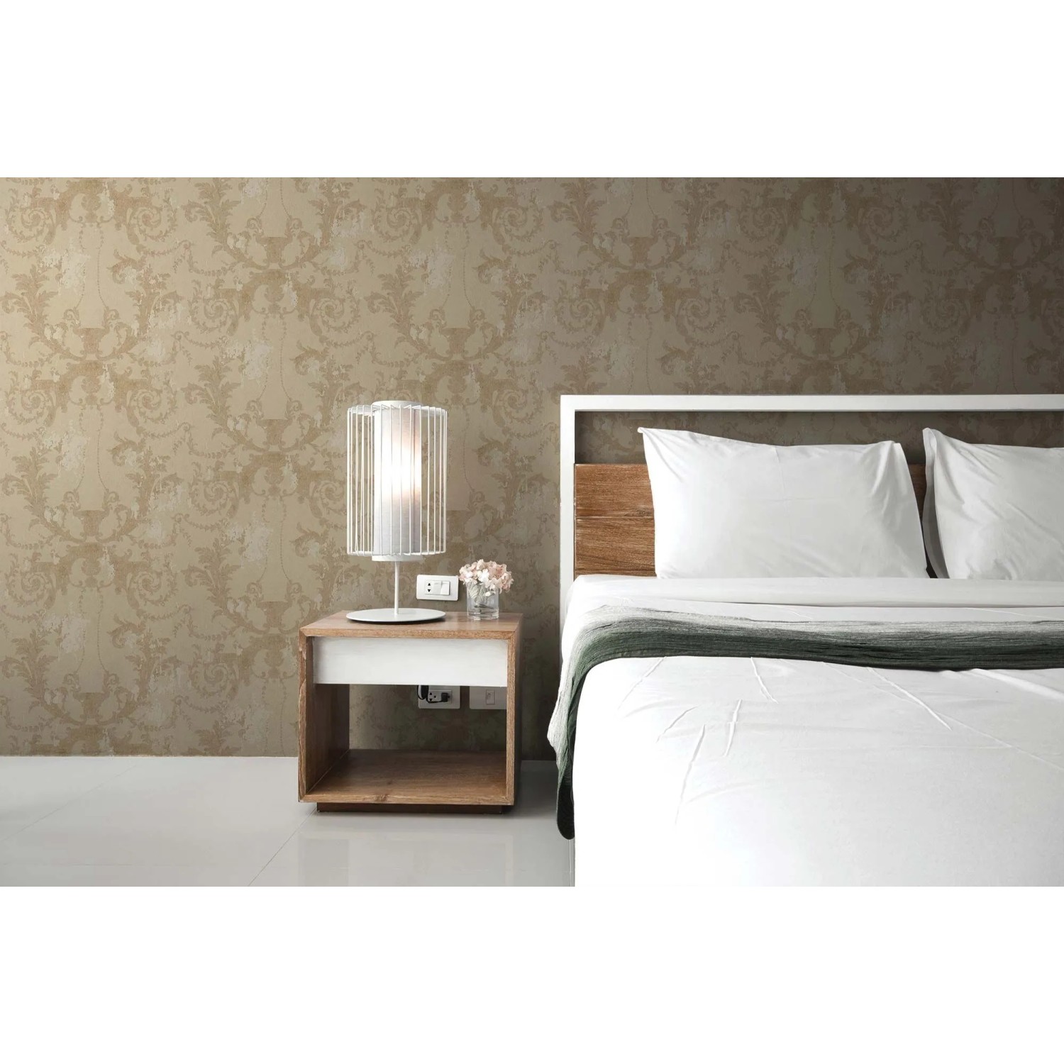 Beige Vliestapete mit barockem Ornamentmuster an einer Schlafzimmerwand, neben einem Bett und Nachttisch.