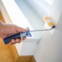 Hand streicht mit LUX Dispersionsroller (12 cm) eine weiße Wand. Farbwalze für glatte Flächen.