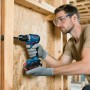 Mann bohrt mit blauem Bosch Professional Akku-Bohrschrauber GSR18V-52 in Holzwand. Trägt Schutzbrille und Handschuhe.
