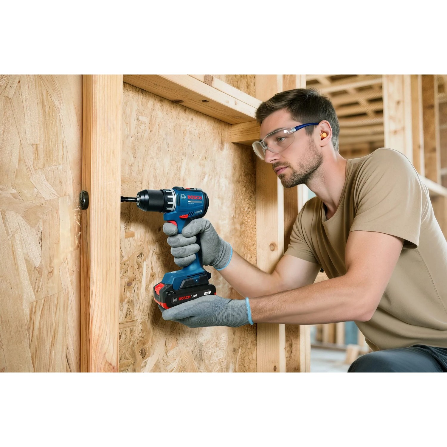 Mann bohrt mit blauem Bosch Professional Akku-Bohrschrauber GSR18V-52 in Holzwand. Trägt Schutzbrille und Handschuhe.