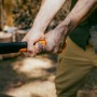Nahaufnahme: Hände halten Fiskars Spaltaxt X32 mit orange-schwarzem Griff. Axt zum Holz spalten.