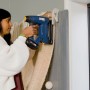 Frau tackert Stoff mit blauem Rapid Akku-Tacker BTX553 an Wand.