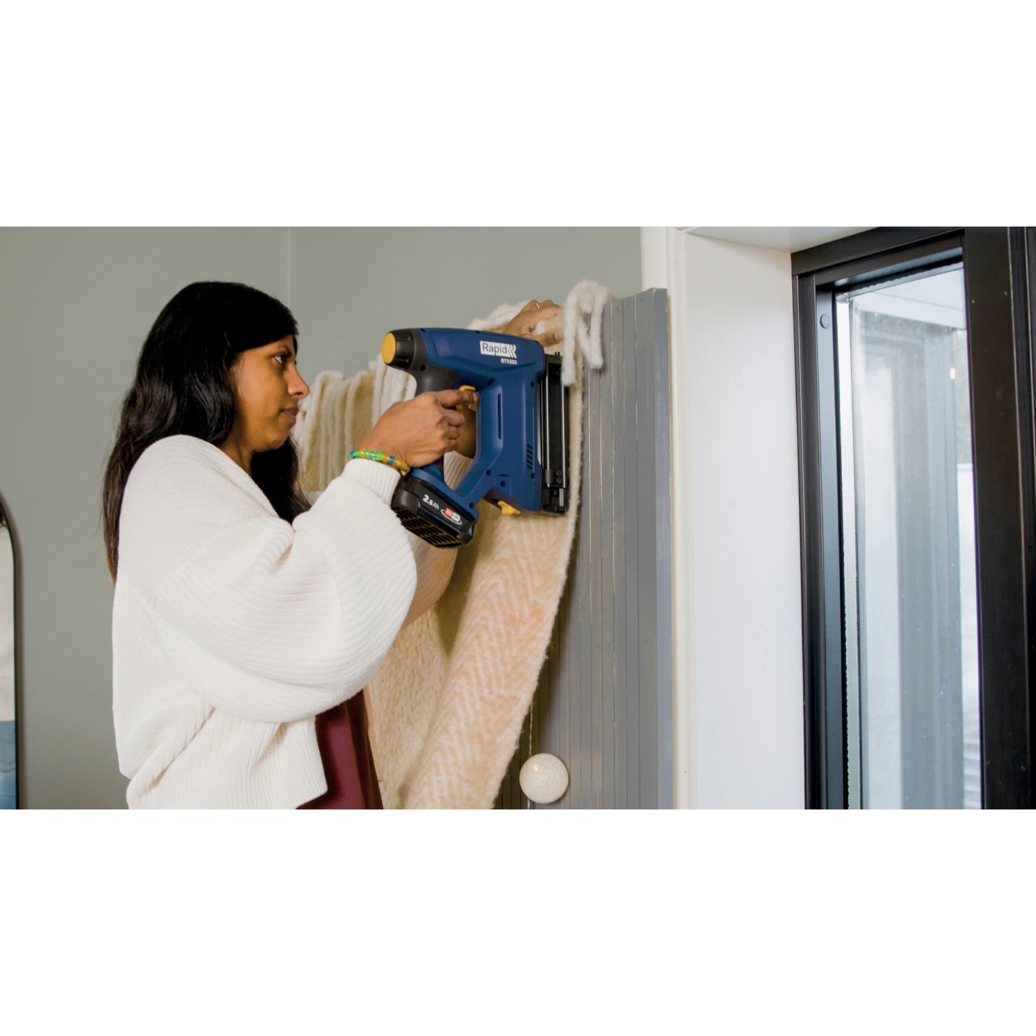 Frau tackert Stoff mit blauem Rapid Akku-Tacker BTX553 an Wand.