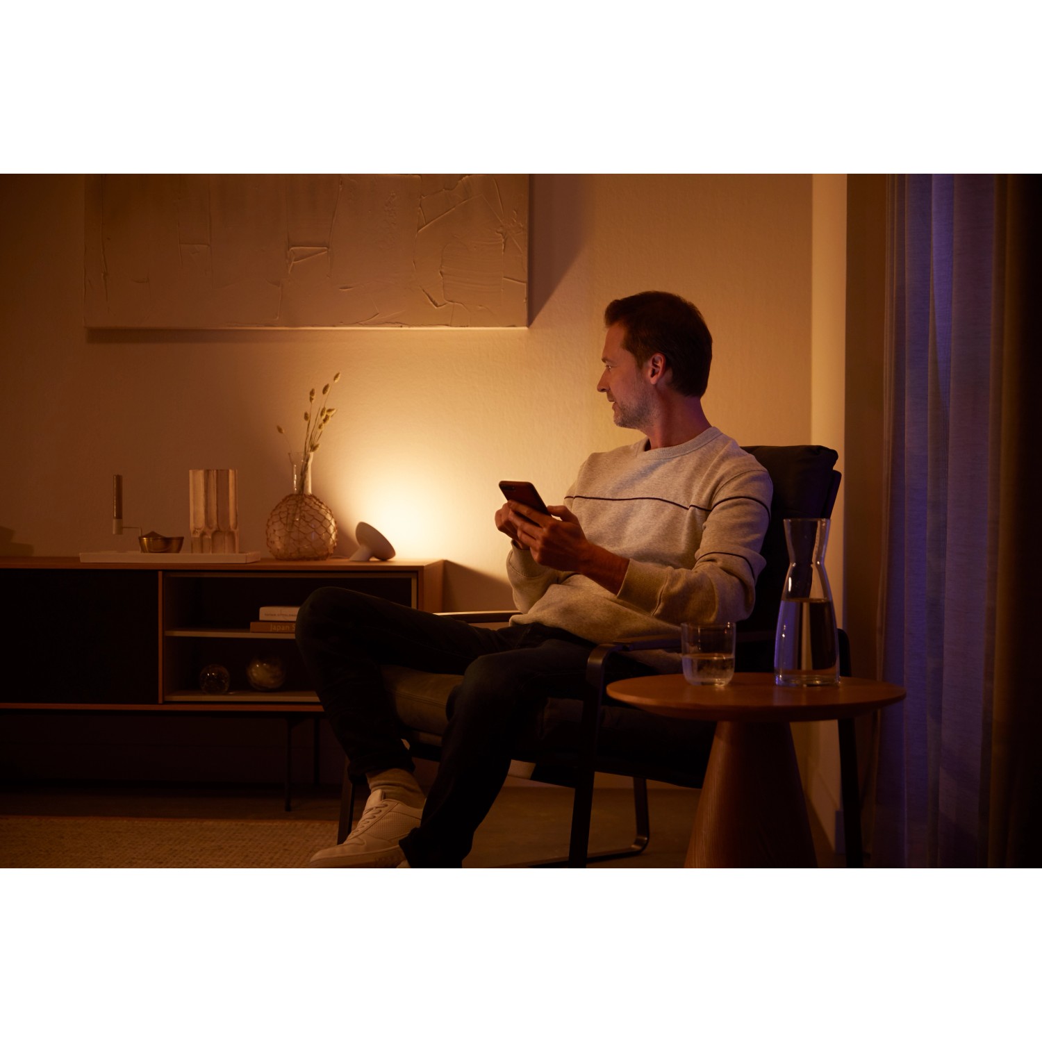 Mann nutzt Philips Hue Bloom Tischleuchte zur Akzentbeleuchtung im Wohnzimmer.