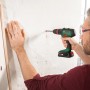 Mann bohrt mit Bosch Akku-Schlagbohrschrauber AdvancedImpact 18 ein Loch in eine Wand.