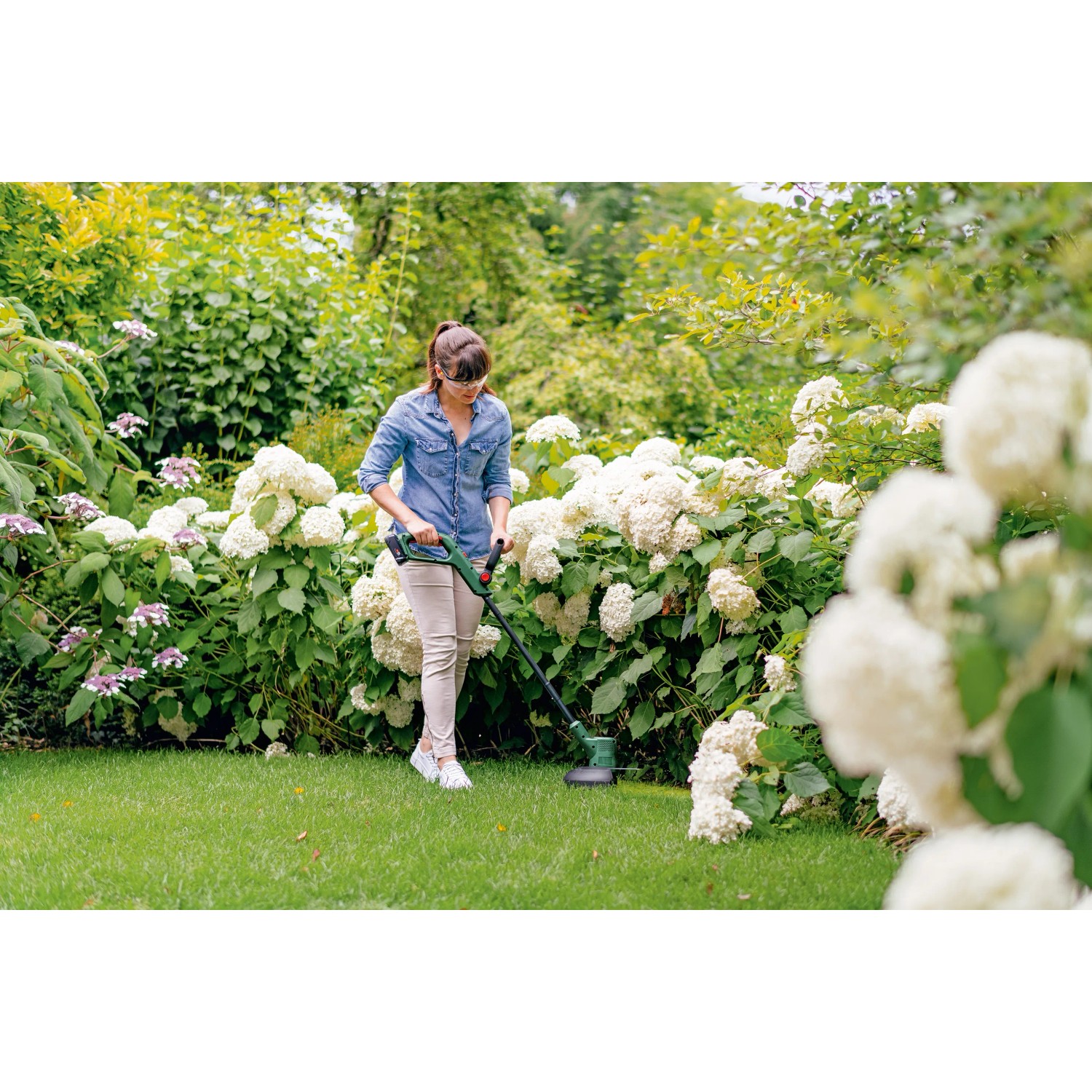 Frau trimmt Rasen mit Bosch Akku-Rasentrimmer EasyGrassCut 18V-230 im Garten.