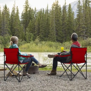 Zwei rote Sunula Campingstühle mit Personen am Flussufer. Ideal für Camping & Outdoor.
