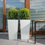 Zwei weiße Siena Garden Pflanzsäulen Nizza mit Rillenoptik, bepflanzt mit grünen Pflanzen.