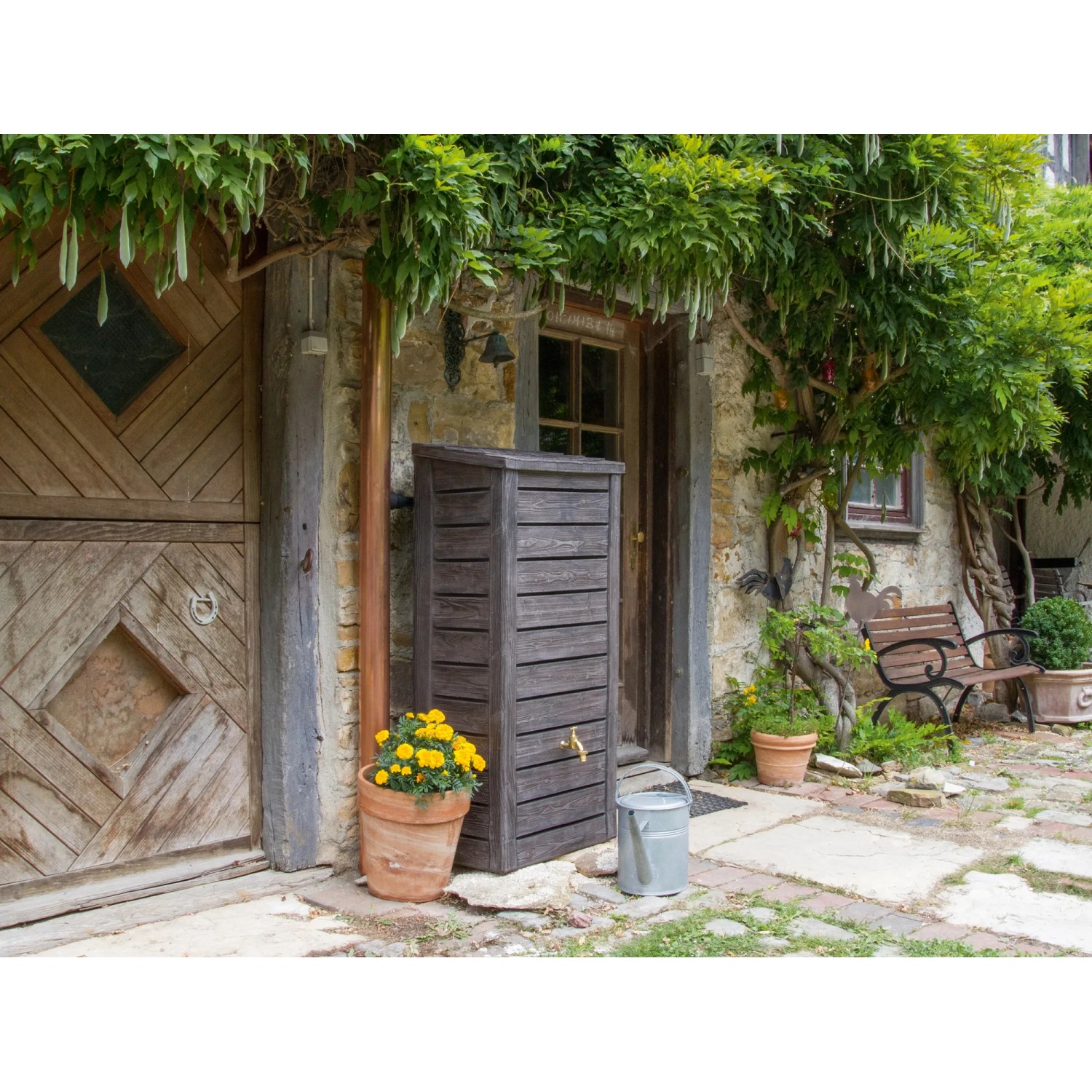 Arves Regentonne Norway 230 l, dunkelbraun, im Garten vor Hauswand mit Pflanzen.
