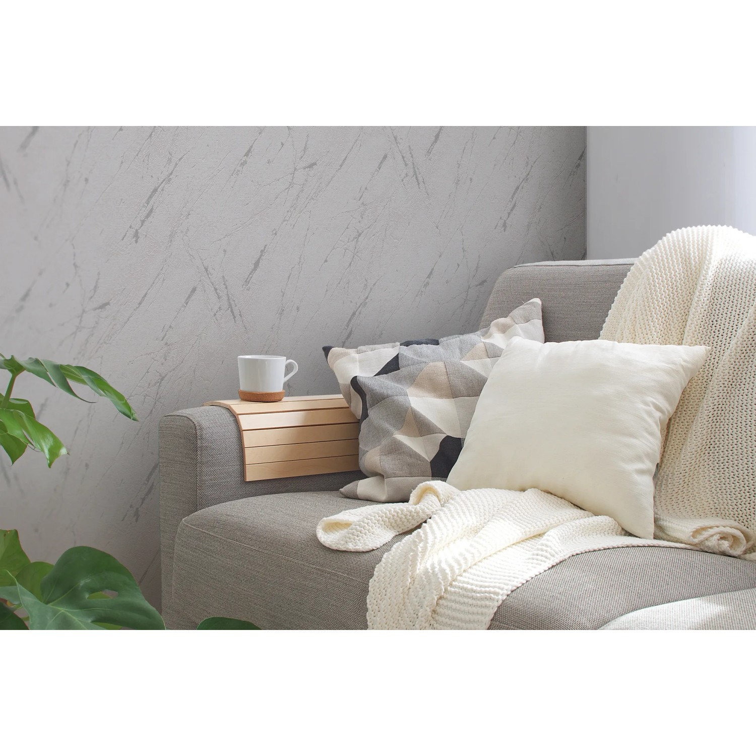 Graue A.S. Création Vliestapete in Marmoroptik an Wohnzimmerwand hinter Couch mit Kissen und Decke.