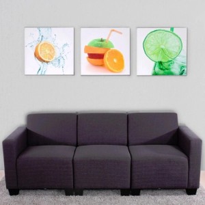 Drei Leinwandbilder mit farbenfrohen Obstmotiven (Orange, Apfel, Limette) über einem Sofa. Modernes Dekoartikel Set.