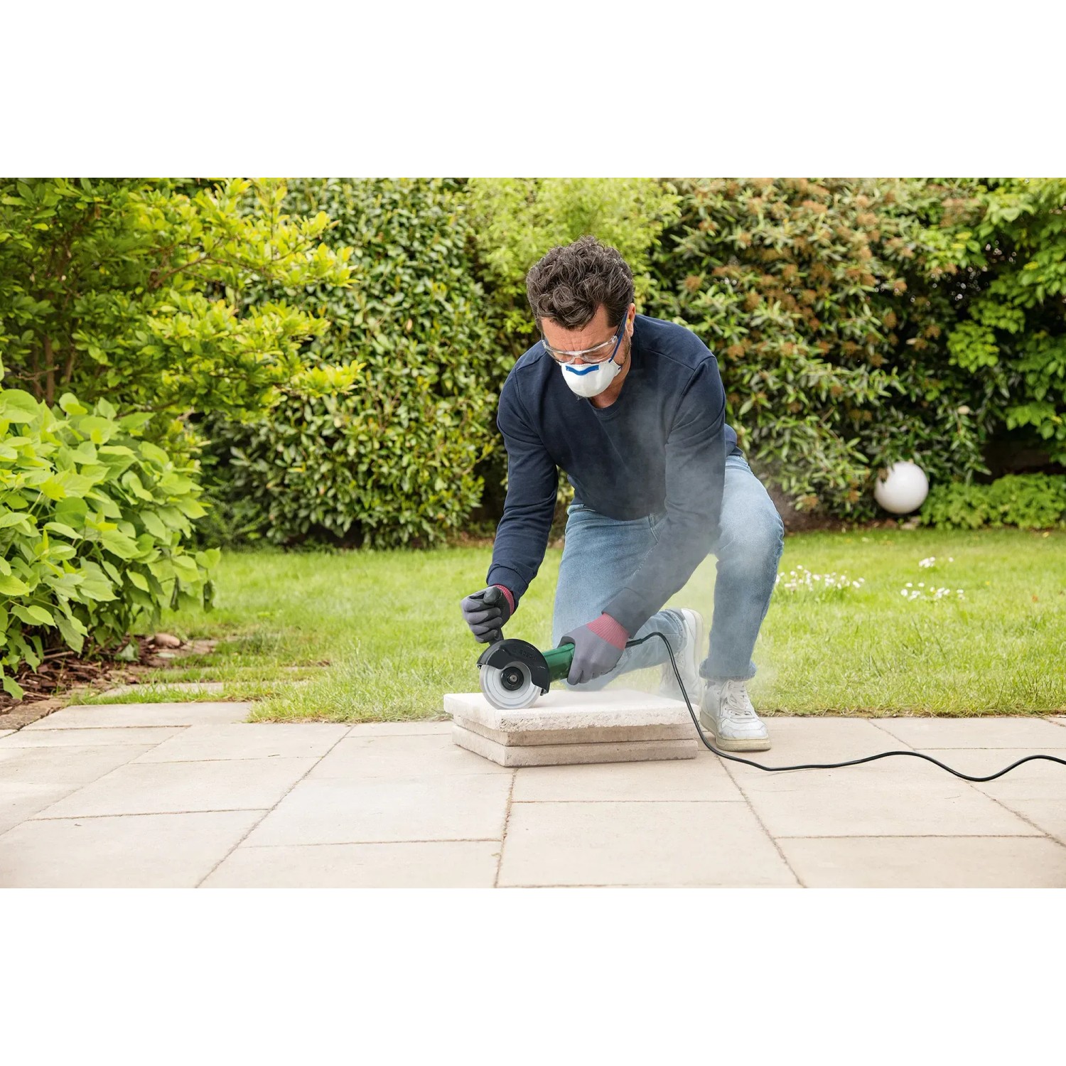 Mann arbeitet mit Bosch UniversalGrind 850-125 Winkelschleifer an Steinplatten im Garten.