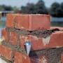 LUX Senklot 250g mit Schnur im Einsatz an einer roten Backsteinmauer. Prüfwerkzeug für senkrechte Ausrichtung.