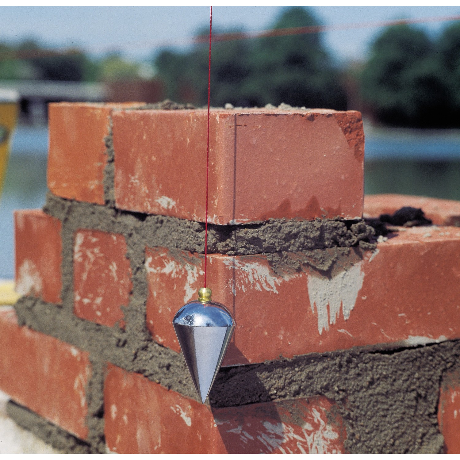 LUX Senklot 250g mit Schnur im Einsatz an einer roten Backsteinmauer. Prüfwerkzeug für senkrechte Ausrichtung.