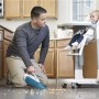 Mann saugt mit Black+Decker Akku-Handstaubsauger Krümel neben Kinderhochstuhl auf.