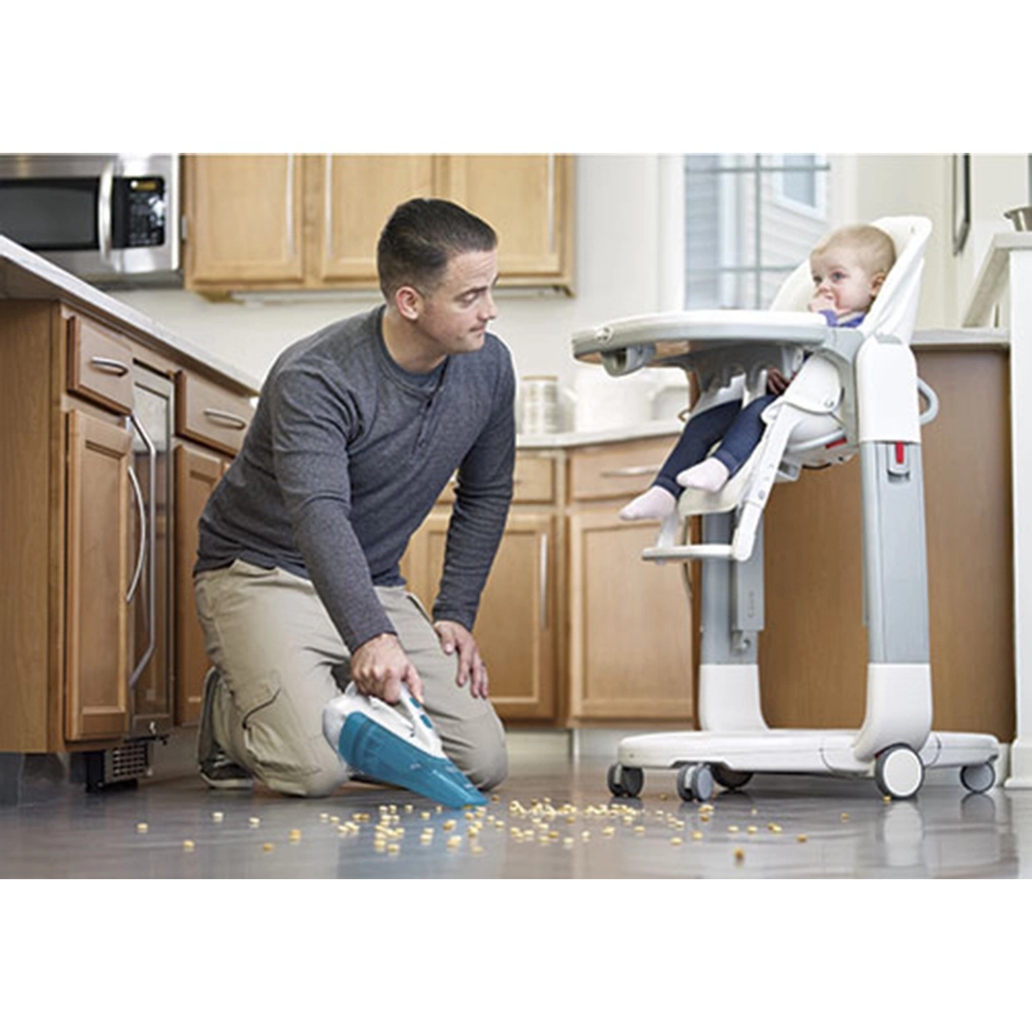 Mann saugt mit Black+Decker Akku-Handstaubsauger Krümel neben Kinderhochstuhl auf.
