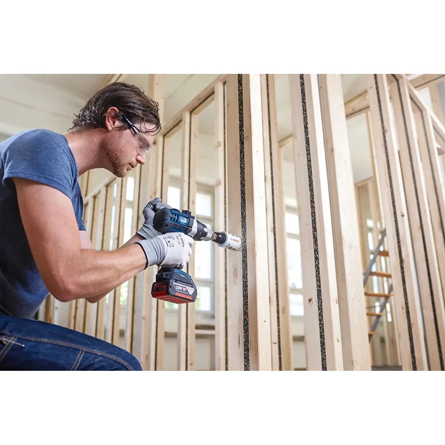 Mann bohrt mit Bosch Lochsäge (83mm) ein Loch in eine Holzwand. Lochsägen für Handwerker.