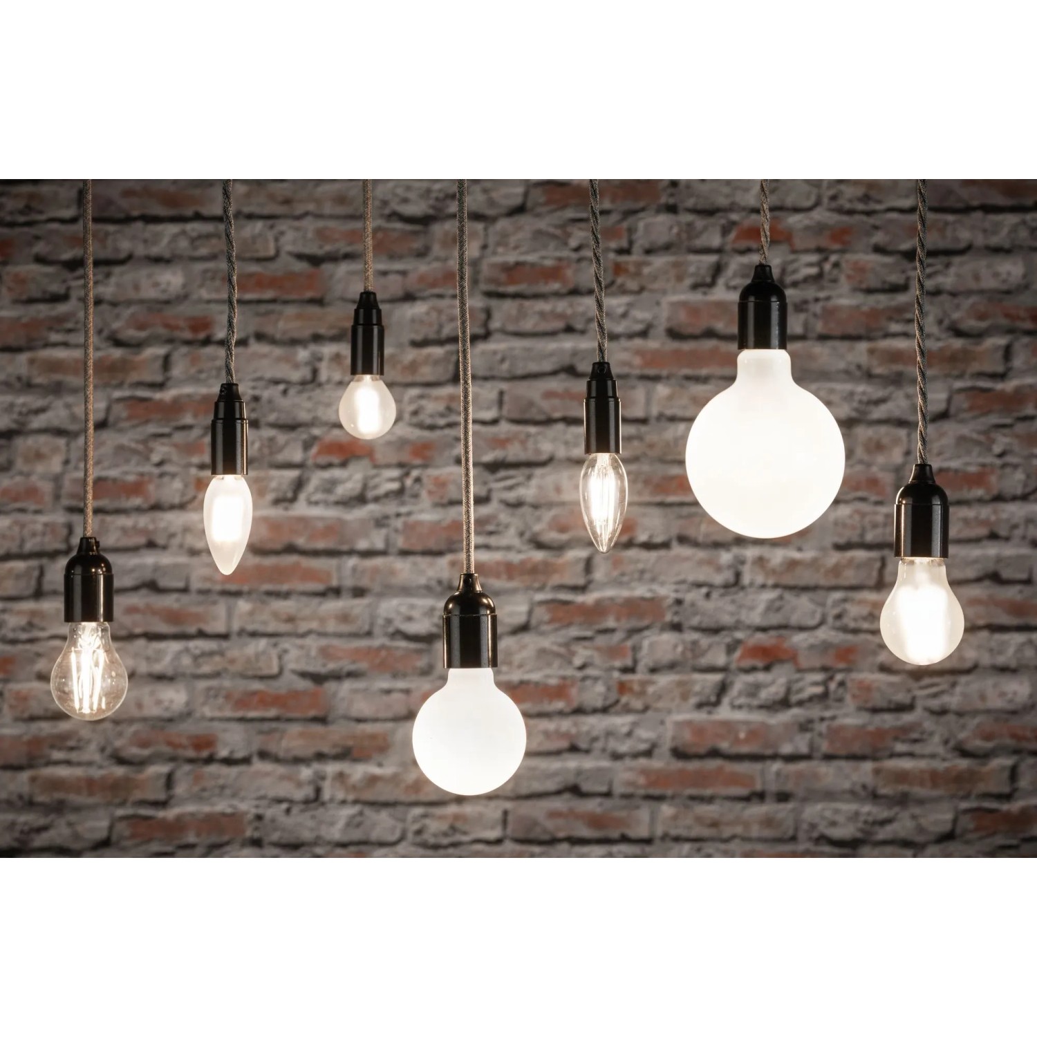 Verschiedene Paulmann E14 LED Leuchtmittel in Tropfenform vor Backsteinwand.