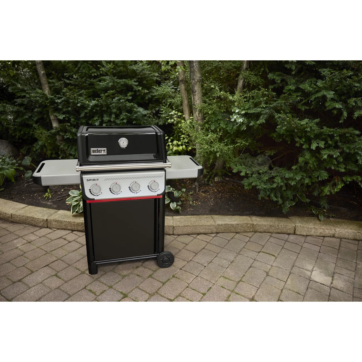 Schwarzer Weber Gasgrill E-410 Spirit mit 4 Brennern und Seitentischen vor Gartenkulisse.