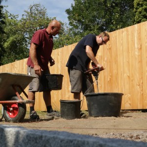 Zwei Handwerker mischen Quick-Mix Ruck-Zuck Beton mit einem Rührer im Freien.