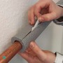 Graue, selbstklebende Scorprotect Rohrisolierung (35x13 mm) wird an einem Rohr befestigt.