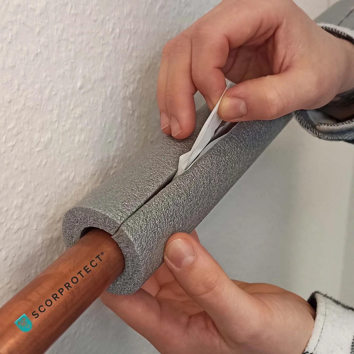 Graue, selbstklebende Scorprotect Rohrisolierung (35x13 mm) wird an einem Rohr befestigt.