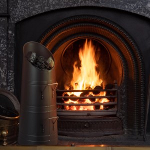 Schwarze Relaxdays Kohlenschütte aus Schmiedeeisen (12 l) neben Kaminfeuer.
