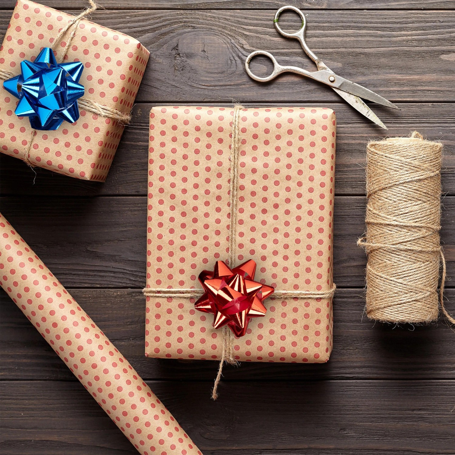 Glänzende rote und blaue Dekoschleifen auf verpackten Geschenken mit Geschenkpapier, Bindfaden und Schere für Weihnachten.