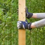 Hände mit LUX-TOOLS Arbeitshandschuhen Soft Protect Plus Gr. 8 halten Holzpfosten im Garten.