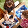 Kinder spielen am Axi Sand- und Wasser-Picknicktisch Nick (braun/blau/weiß) mit Sand.