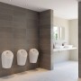 Drei weiße Ideal Standard Urinale im modernen Badezimmer mit Waschbeckenarmaturen.