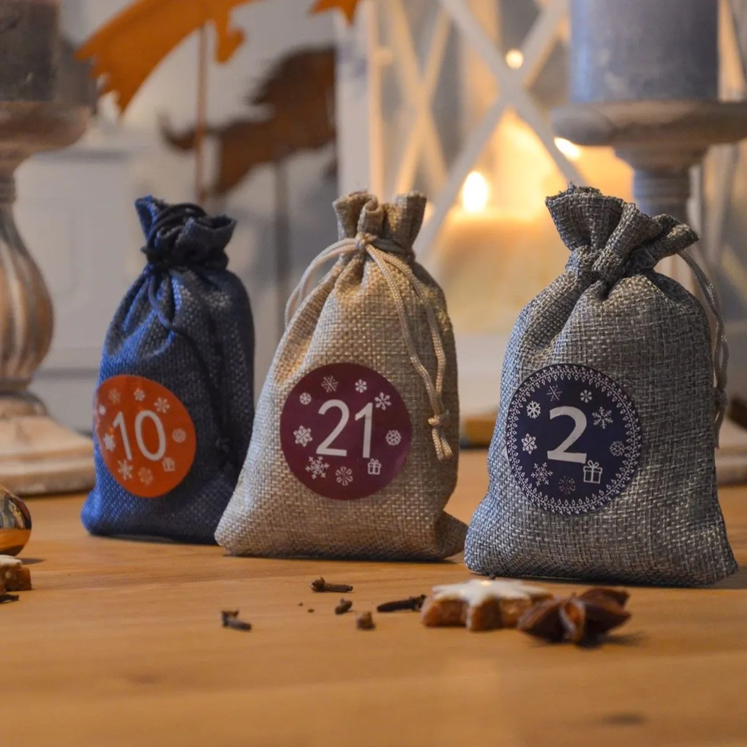 Drei DIY Adventskalender Säckchen (blau, beige, grau) mit Zahlenstickern auf Holztisch, festlich dekoriert. Ideal zum Befüllen.