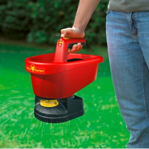 Wolf-Garten Universal-Streuer WE-B in Nutzung: Roter Streuwagen verteilt Saatgut auf Rasen.